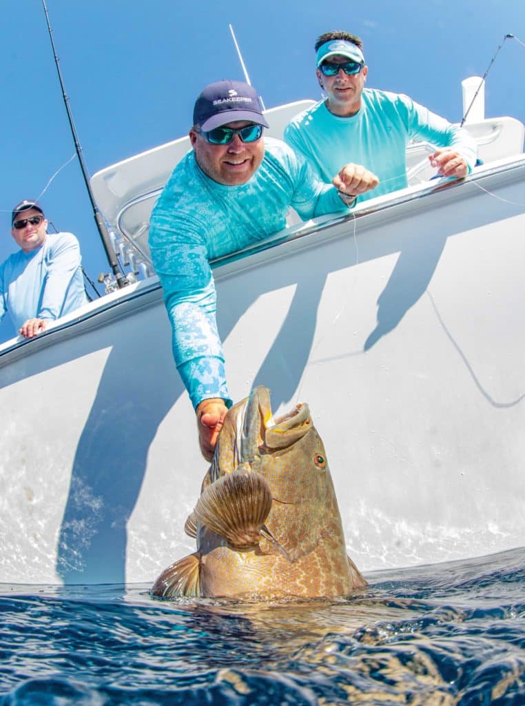 Smiling fisherman pulling in black grouper