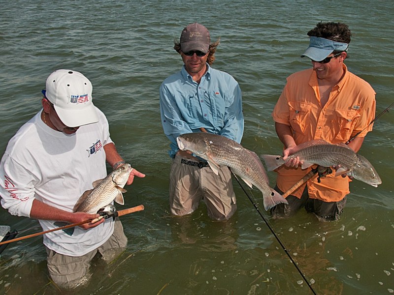 Three wading anglers with redfish caught on lures